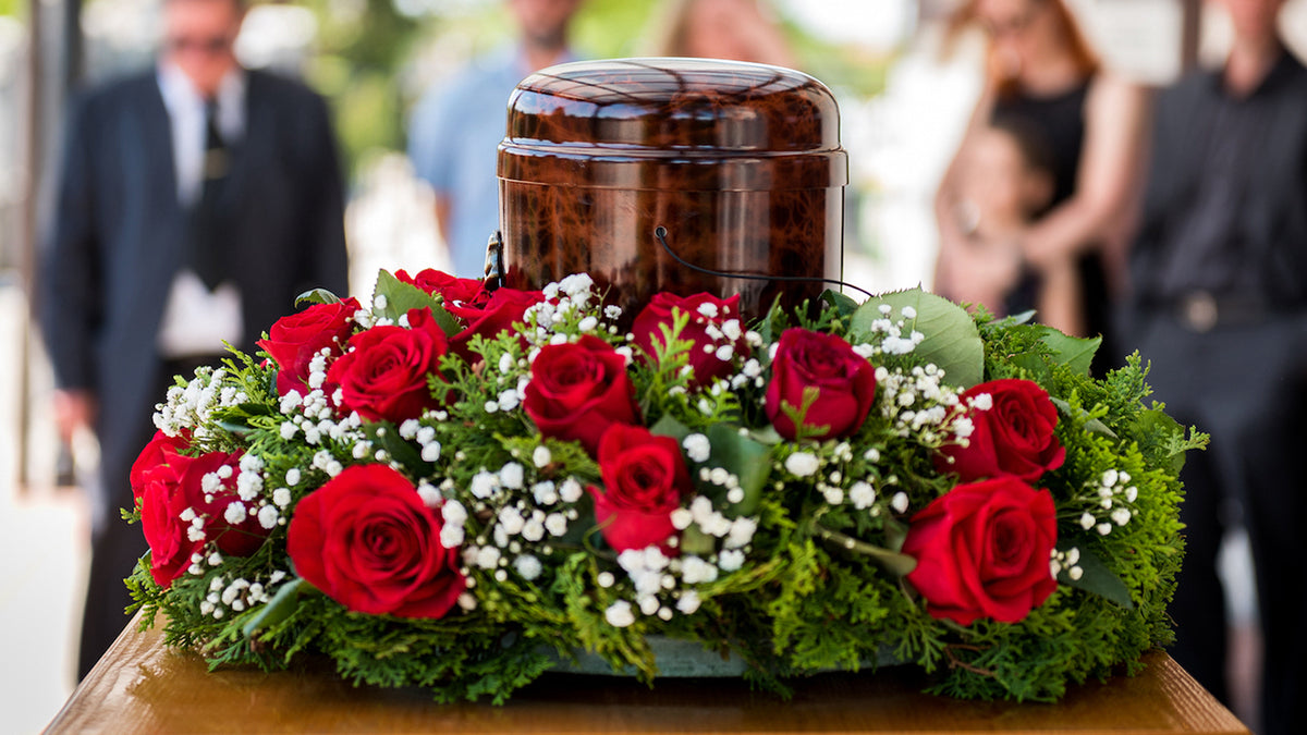 Urne funéraire entourée de roses rouges lors d’une cérémonie commémorative en extérieur.